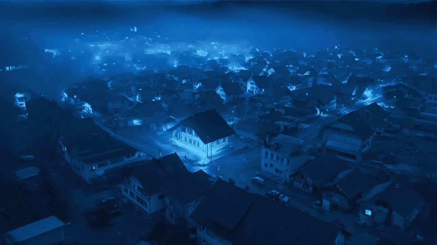 Schweizer Dorf bei Nacht von oben, ein einzelnes Gebäude warm beleuchtet